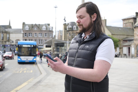Man looking at a mobile phone with a bus in the background