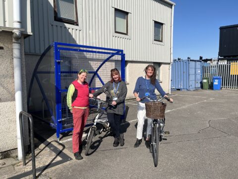 Sheila Wickens (HITRANS) and Tammy Campbell and Jaci Douglas from CALA with the new secure cycle shelter at the CALA office in Inverness